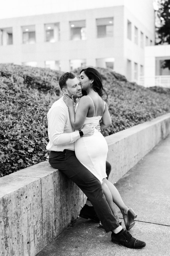 girls whispers into guys ear as he leans against wall