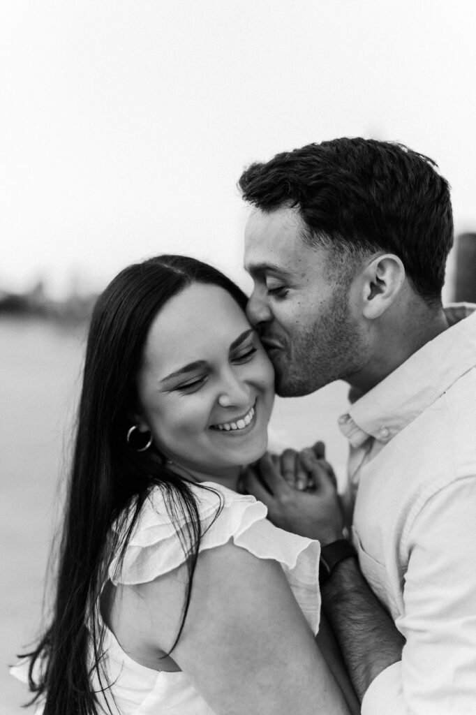 Man kisses woman's forehead during cityscape engagement in Atlanta, GA.