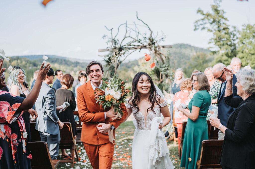 Bride and Groom walk down aisle as guests throw flowers. Wedding at Flat Rock Farms.
