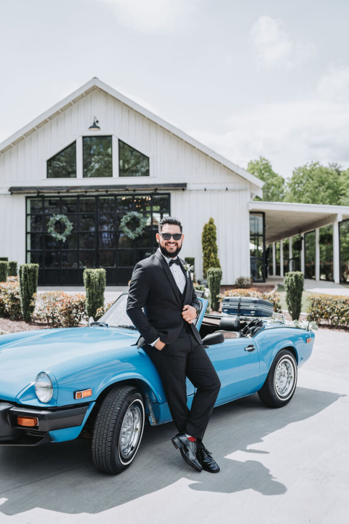Groom leans against blue vintage car