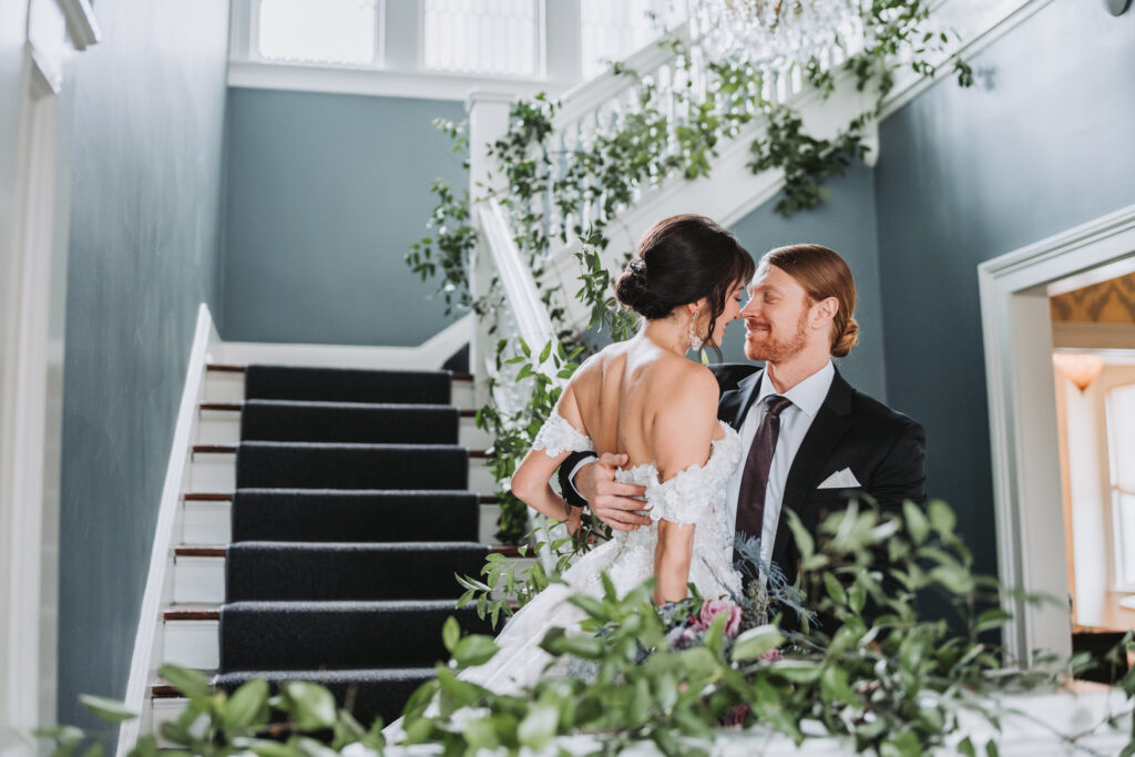 Bride and groom look at each other on floral stair case