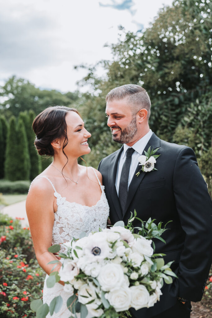 bride and groom smile at each other while holding flowers on their wedding day.