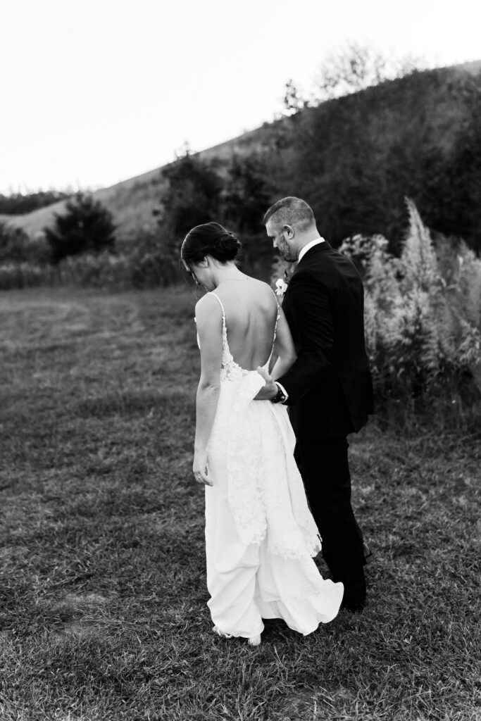 Groom holds bride's dress as they walk.