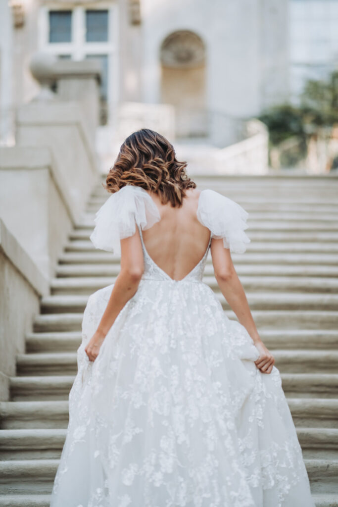 Bride runs up the staircase of the swan house. Her back is towards the camera