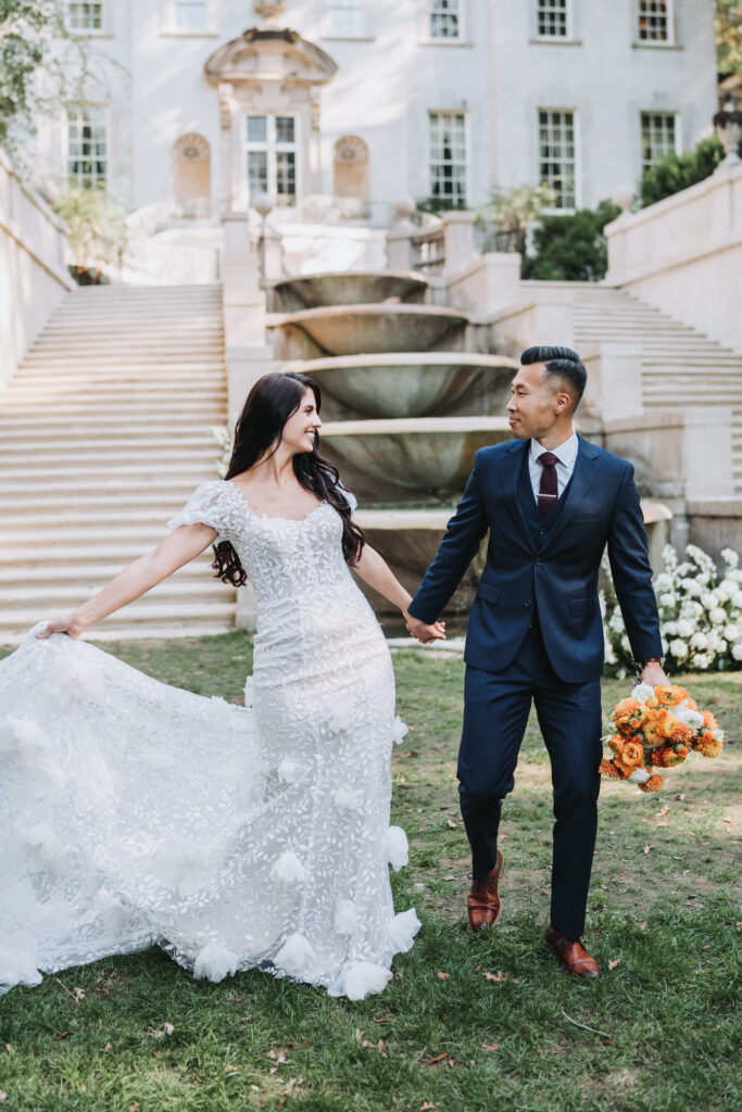 Bride and Groom walk towards camera hand in hand. Swan house is in the background.