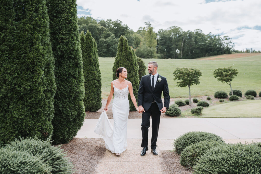 Bride and groom walk while holding hands.