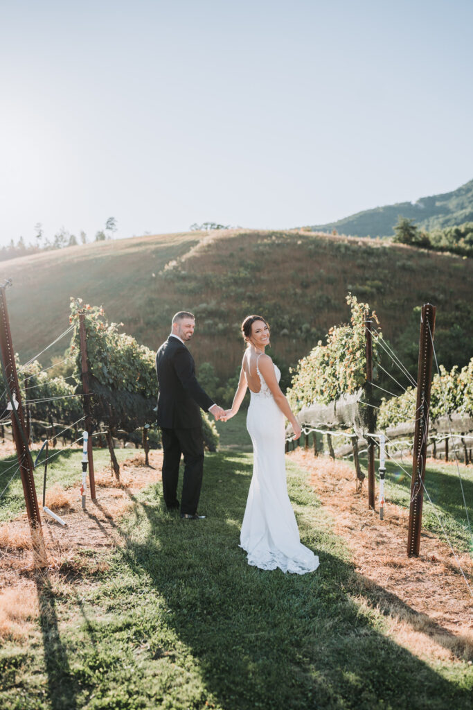 Bride looks back over her shoulder while walking with groom. Yonah Mountain is in the background.