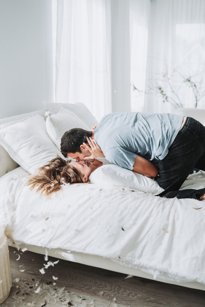 woman and man kiss on bed after their pillow fight engagement session