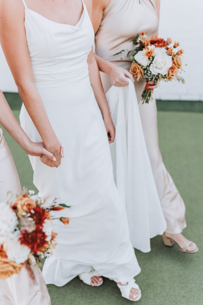 bride and bridesmaids hold hands while walking with fall bouquets.