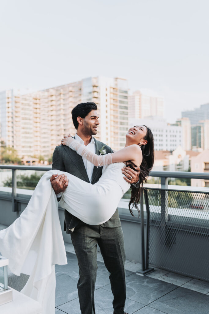 Groom picks up bride like a baby. Atlanta skyline is the background.