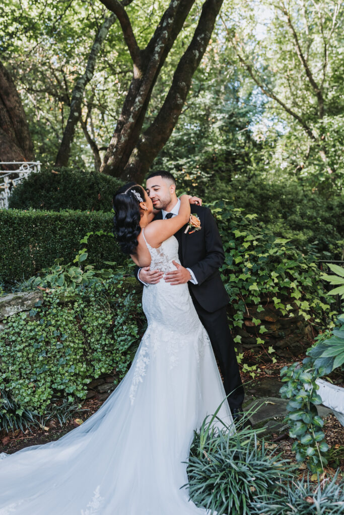 Bride and groom hold each other. Bride's wedding dress is lacey with thin straps from Aisle & Veil.