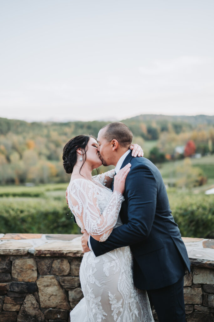 Bride and groom kiss on wedding day with Crane Creek Vineyards in the background.