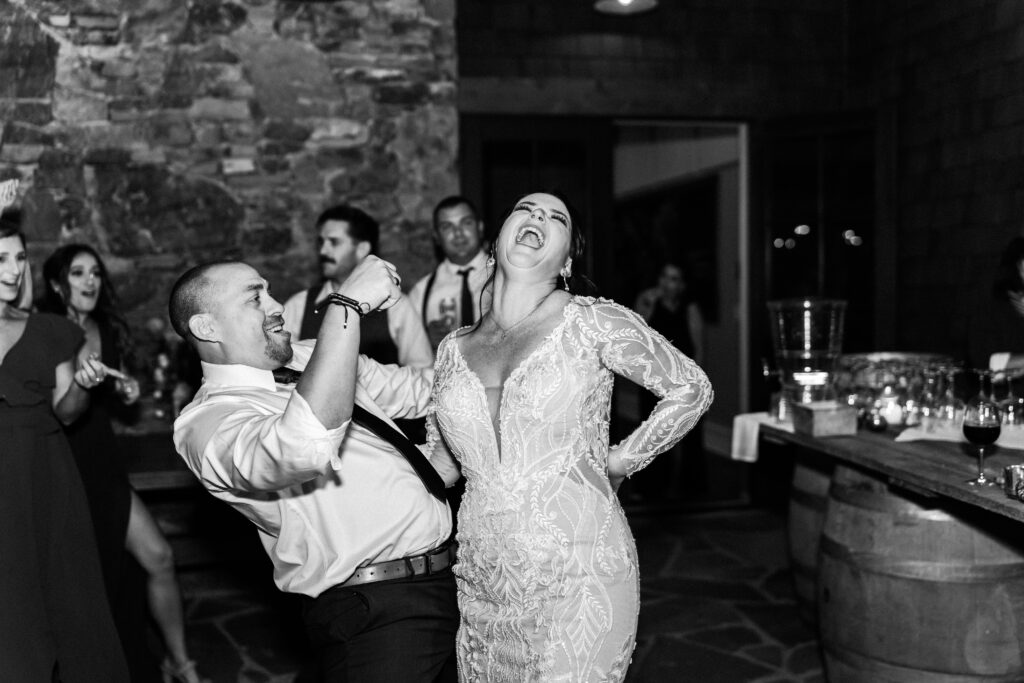 bride and groom dance with each other. She laughs.