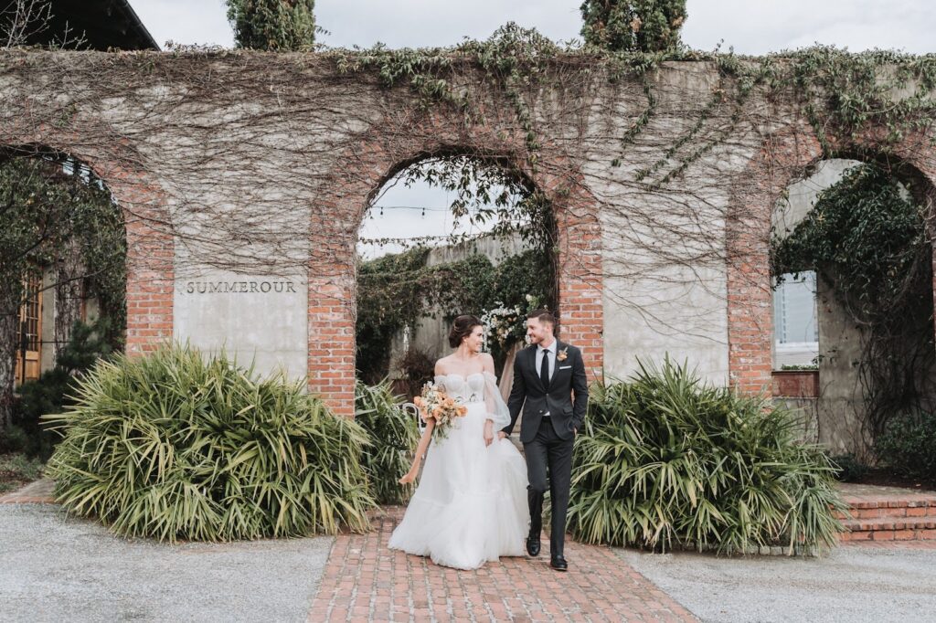 Bride and groom walk towards camera with Summerour wedding venue in the background