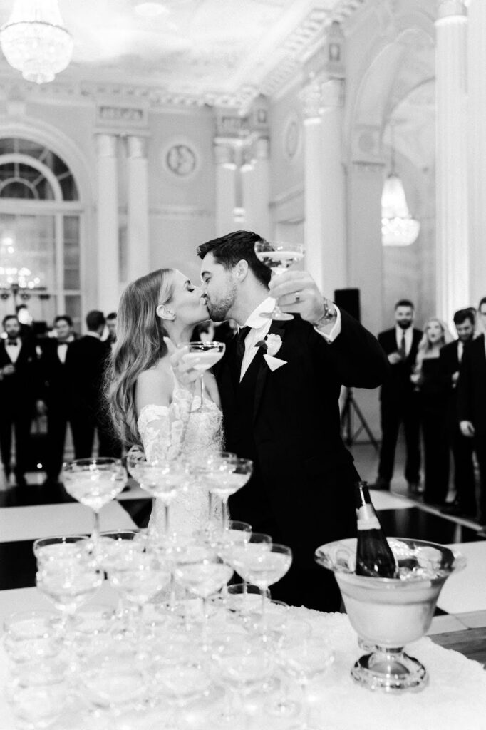 bride and groom kiss while holding champagne glasses