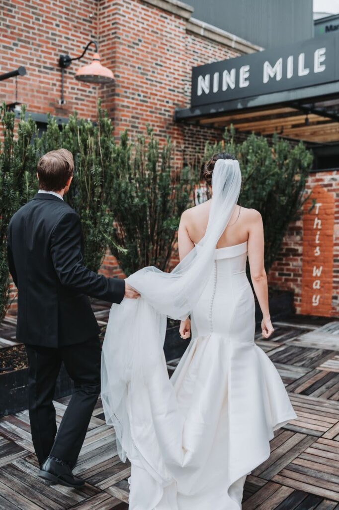 Groom holds bride's dress as they walk along Ponce City Rooftop