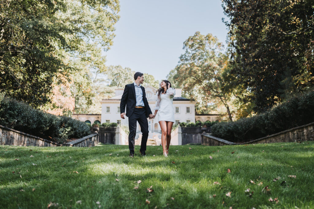 guy and girl run towards camera with the Swan House Atlanta History Center in the background.