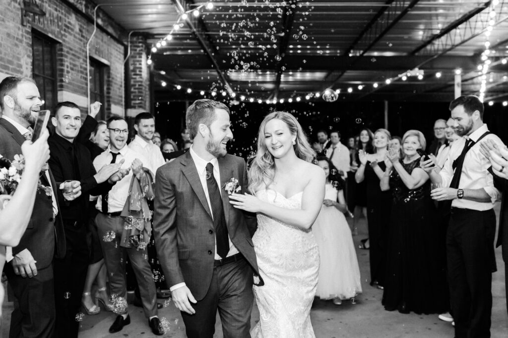 bride touches grooms chest as they leave Guardian works wedding venue. They have a bubble exit.