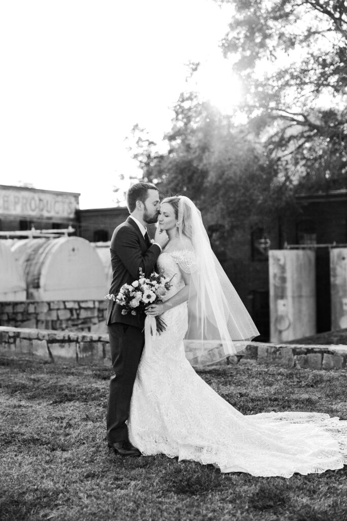 Groom holds bride's chin and kisses her cheek.