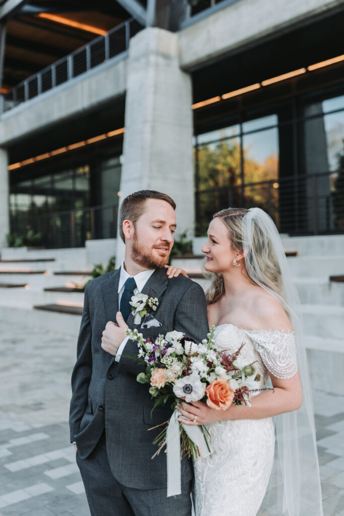 Bride holds grooms shoulder and they look at each other