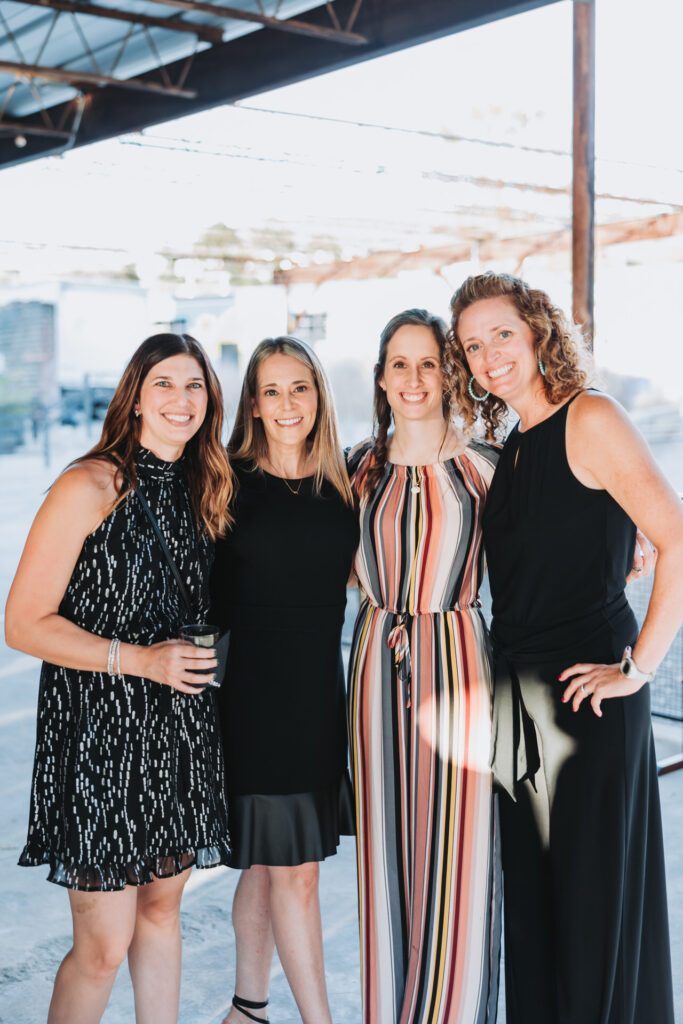 four women smile at the camera during cocktail hour