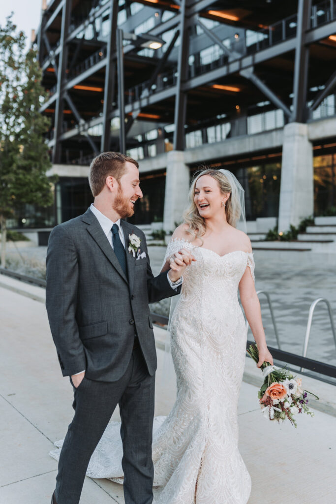bride and groom laugh as they walk hand in hand.
