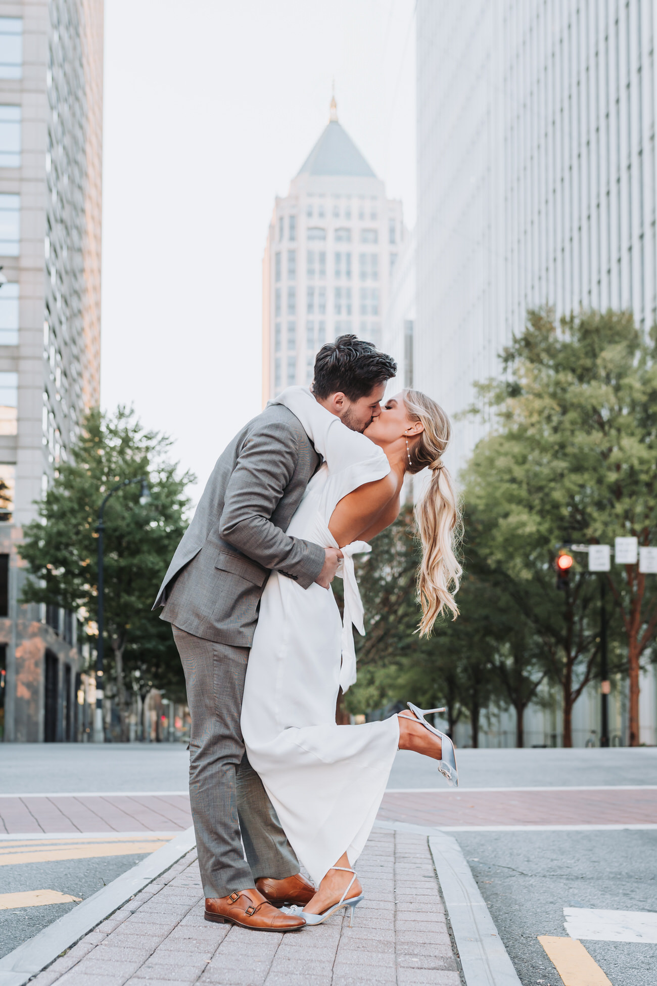 Guy dips girl back and kisses her on atlanta street. Buildings can be seen in the background.