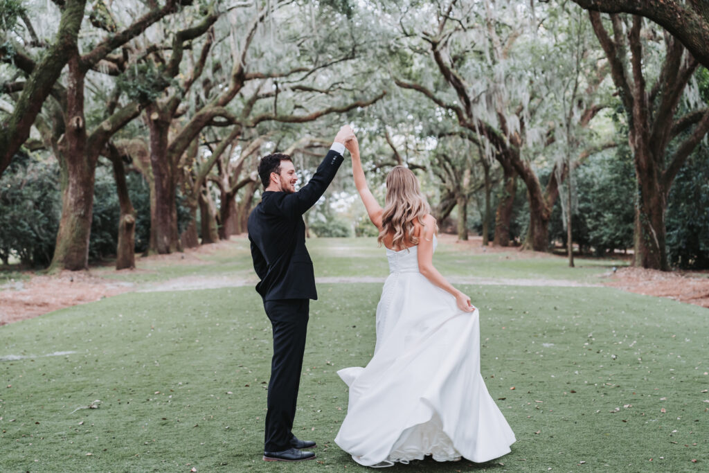 Groom twirls bride under the Avenue of Oak trees at Legare Waring house wedding venue