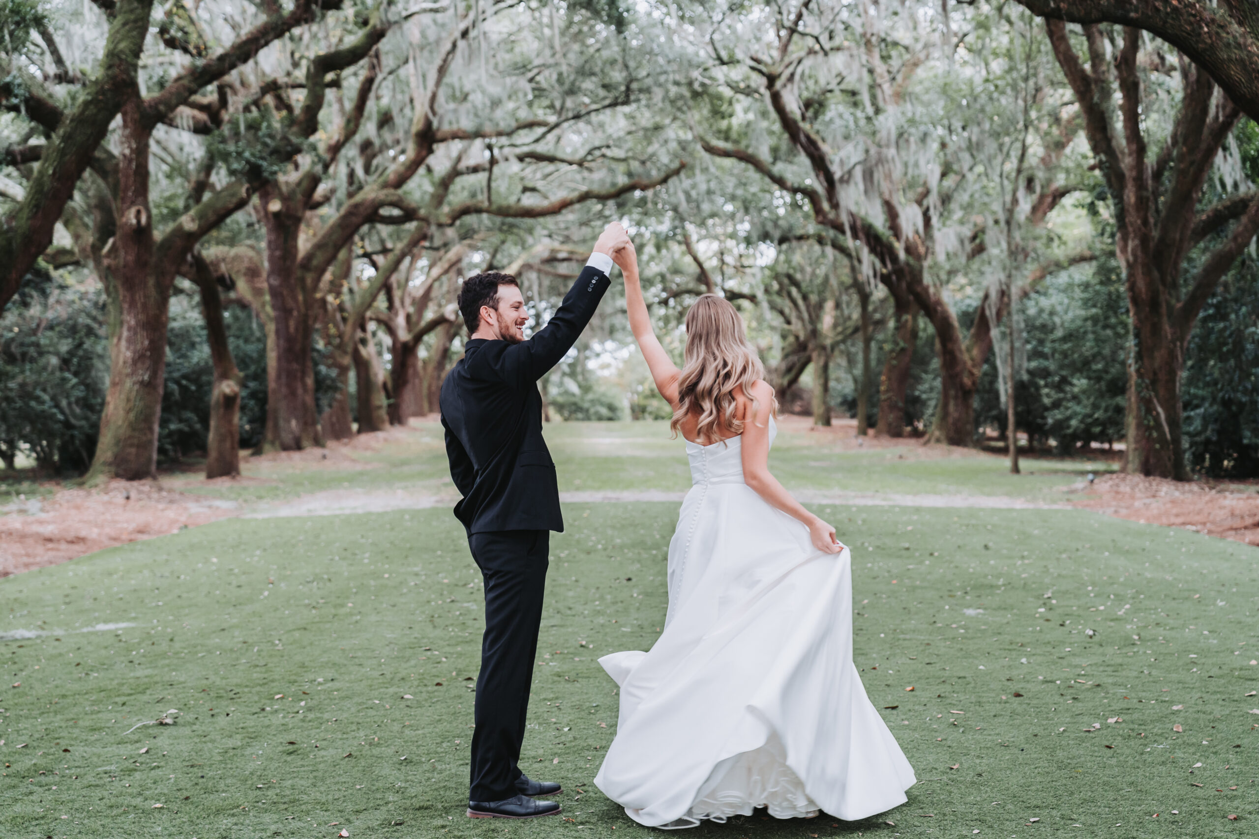 Groom twirls bride under the Avenue of Oak trees at Legare Waring house wedding venue