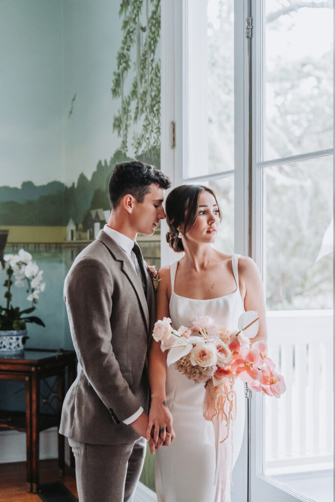 Groom holds bride's waist as she looks out the window