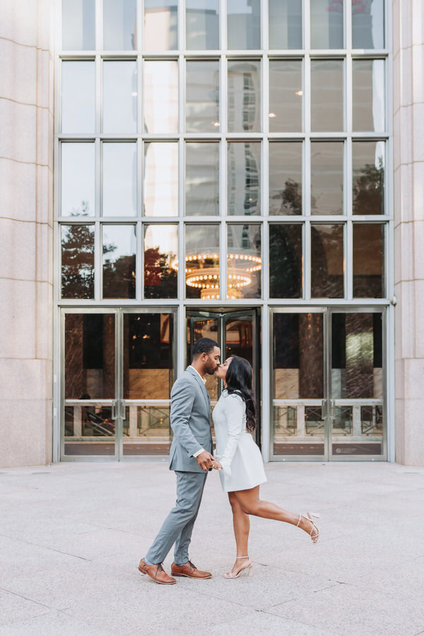 Couple kisses in front of Atlanta city building. 