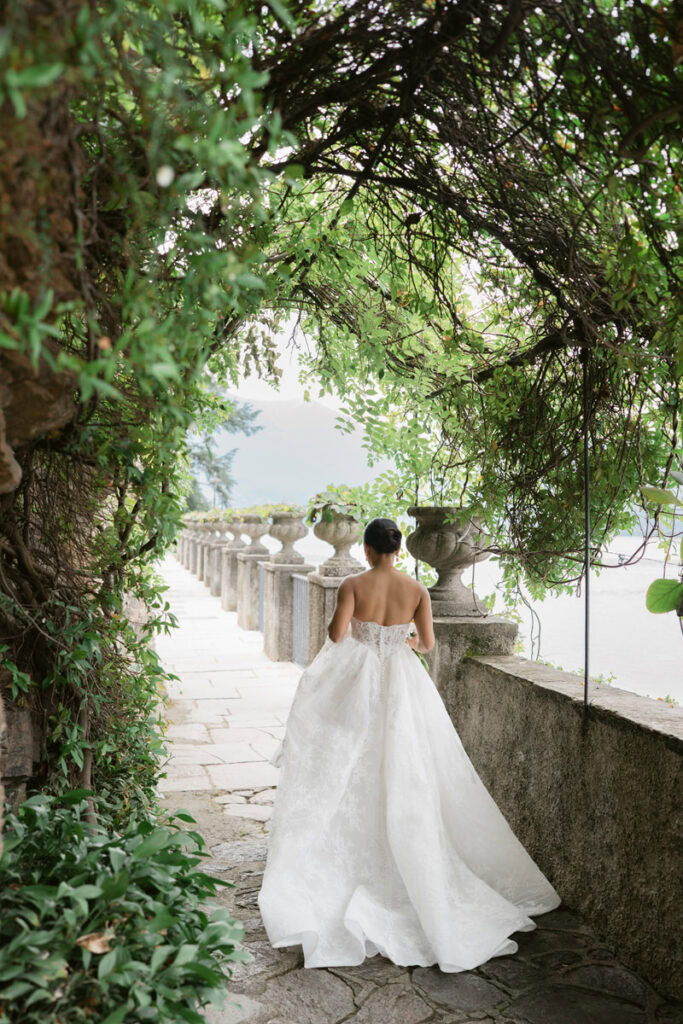 Elegant photo of bride walking through arch way filled with greenery 